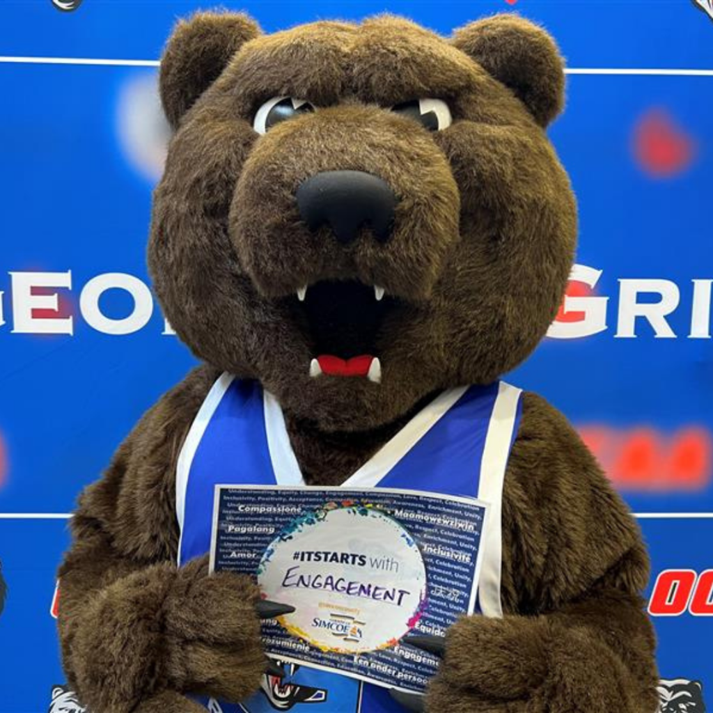 Grizzly Growler (Georgian grizzly bear mascot) holds up a paper in front of a blue background.