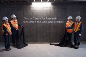 Four people with hard hats and safety vests unveiling the sign that says Alectra Centre for Research, Innovation and Commercialization