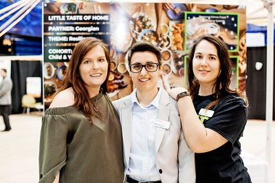 Three female changemaking students standing in front of a display of their changemaking project NOURISH
