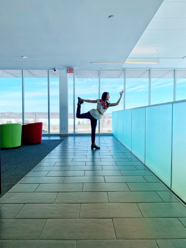 Person poses in a yoga position in front of ceiling to floor windows at Georgian College.