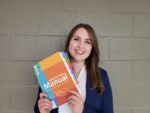Danielle, Writing Technologist, long brown hair, smiling at camera, holding a copy of the APA Publication Manual