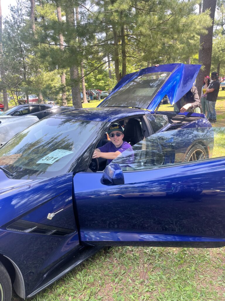 Man in purple shirt and and hat sitting in a blue car.