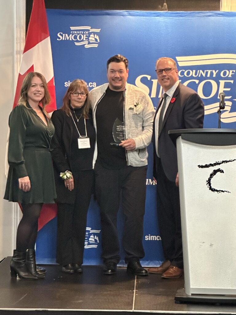 Four people standing side by side with individual second from right holding an award.