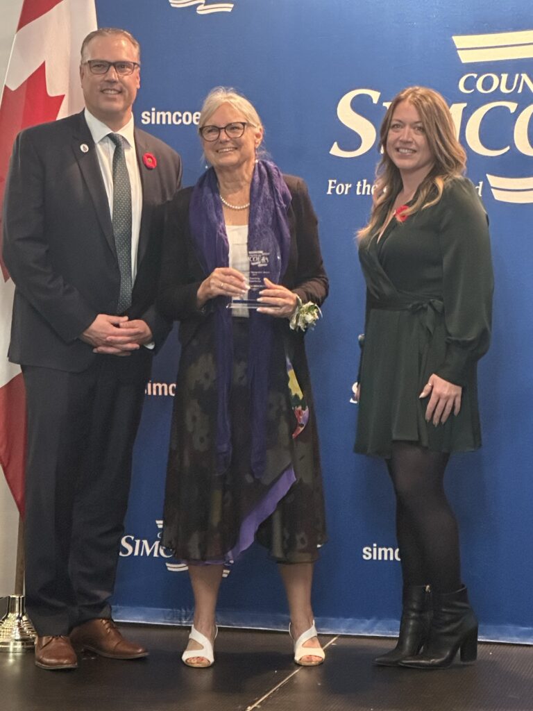 Three people standing side by side with middle individual holding an award.