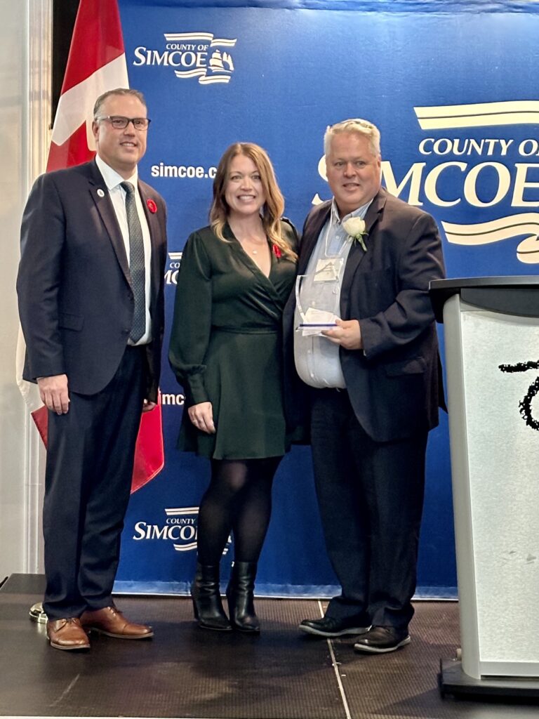 Three people standing side by side with the individual on the right holding an award.