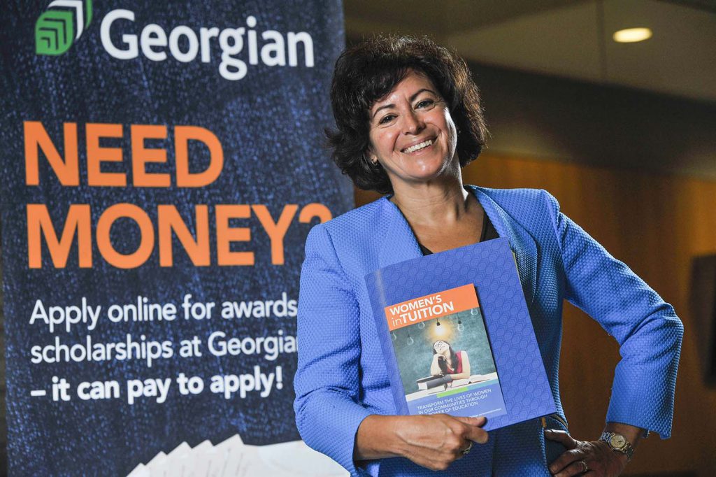 Giselle Bodkin holds the WOMEN'S inTUITION pledge form, standing in front of a sign that reads "Need money?"