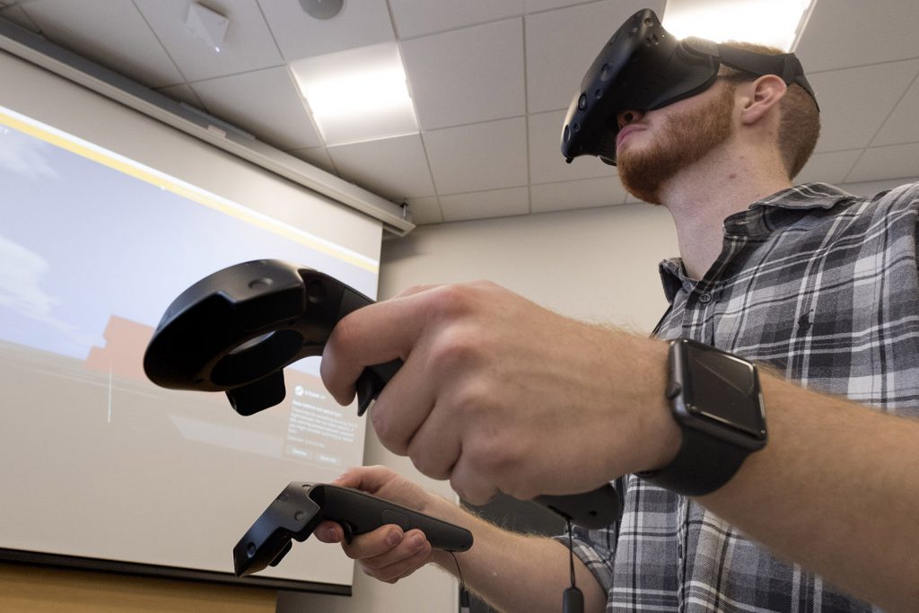A man wearing a virtual reality mask and holding a remote control in each hand.