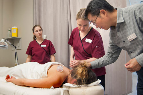 2 students with professor performing acupuncture treatment