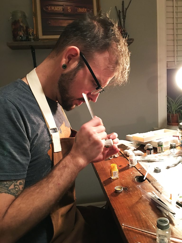 Person sitting at a table and painting a sculpture.
