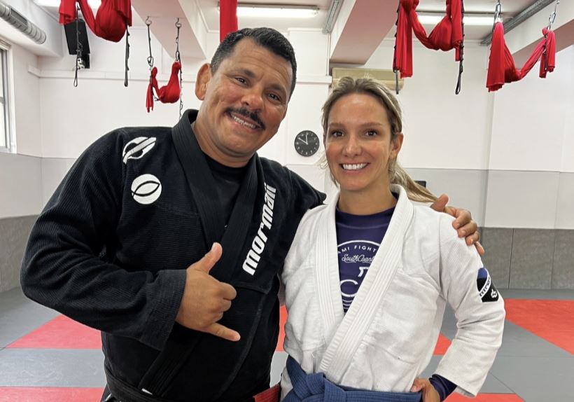 Two people wearing martial arts uniforms stand next to each other and smile in a gym.