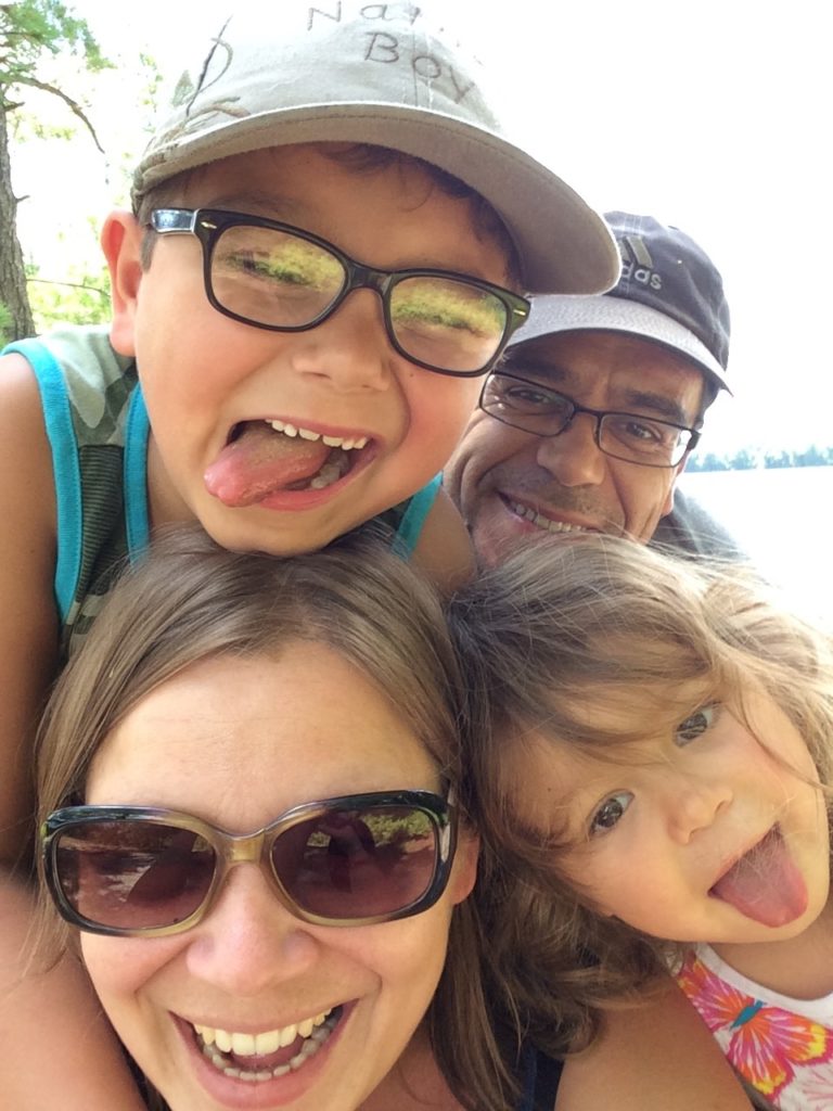 Two adults and two kids smile and stick their tongues out in a group selfie.