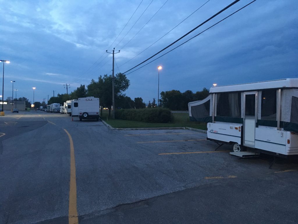 A row of tent trailers are parked at night in a parking lot.
