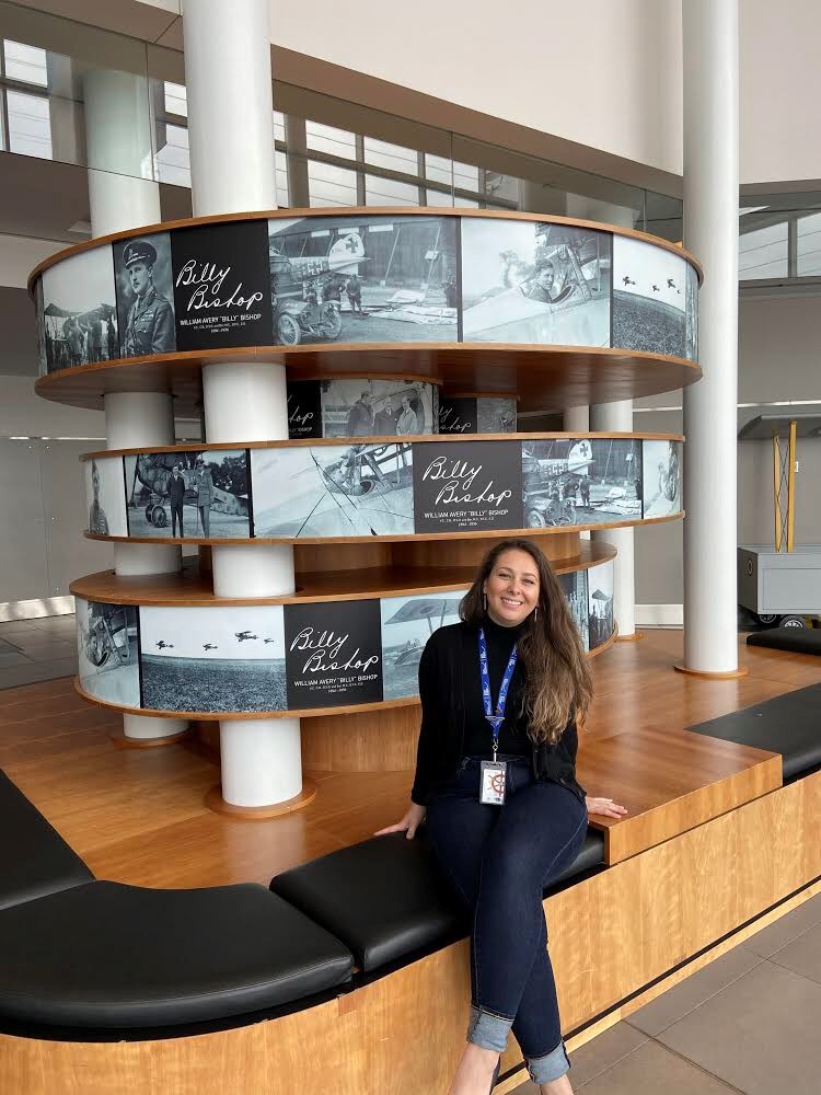 Person smiles at the camera while sitting on a bench inside a building.