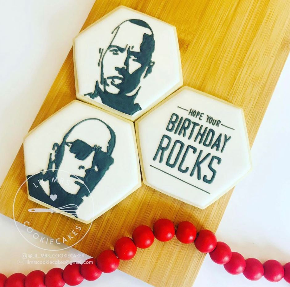 Aerial view of three sugar cookies decorated with images of actor Dwayne "The Rock" Johnson. Text: Hope your birthday rocks.