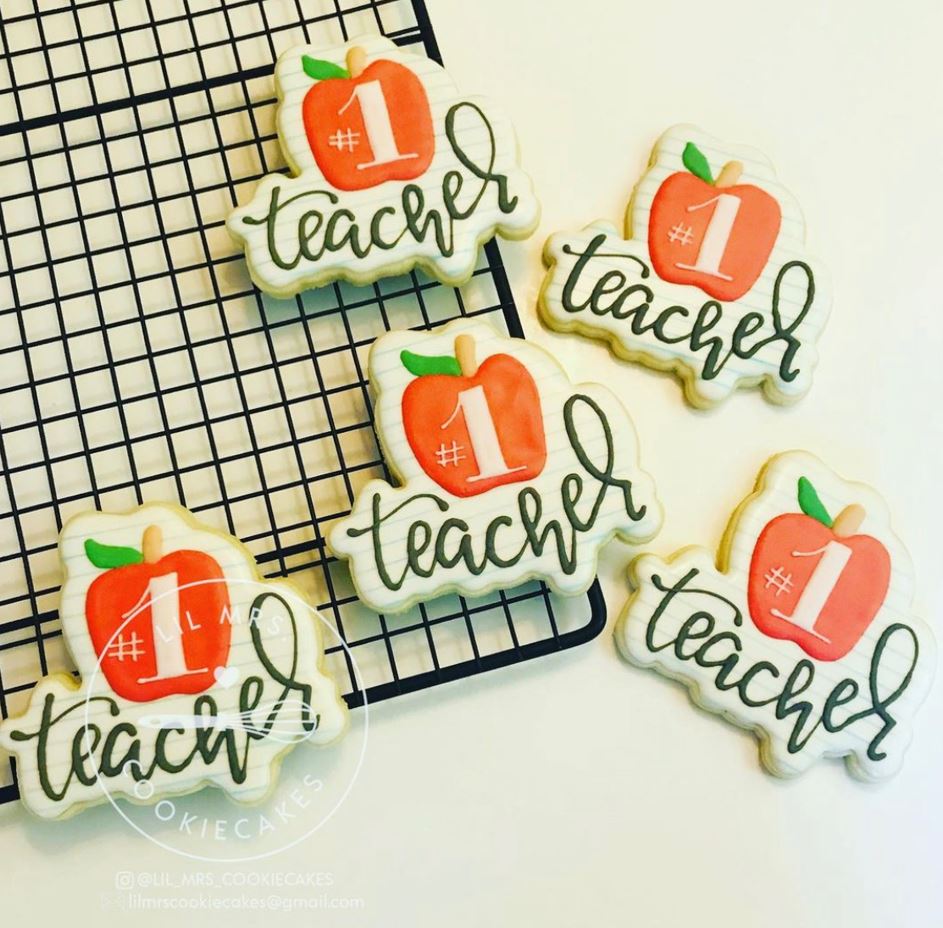 Aerial view of five sugar cookies decorated with a design featuring an apple and the words #1 teacher.