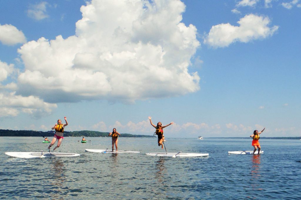 Four girls jump on their paddleboards while out on the lake