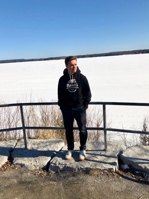 A young man wearing a blue track suit leaning against a fence with frozen water in the background