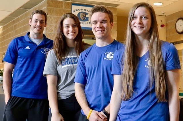 Four young people smiling at the camera - two males and two females dressed in athletic clothing