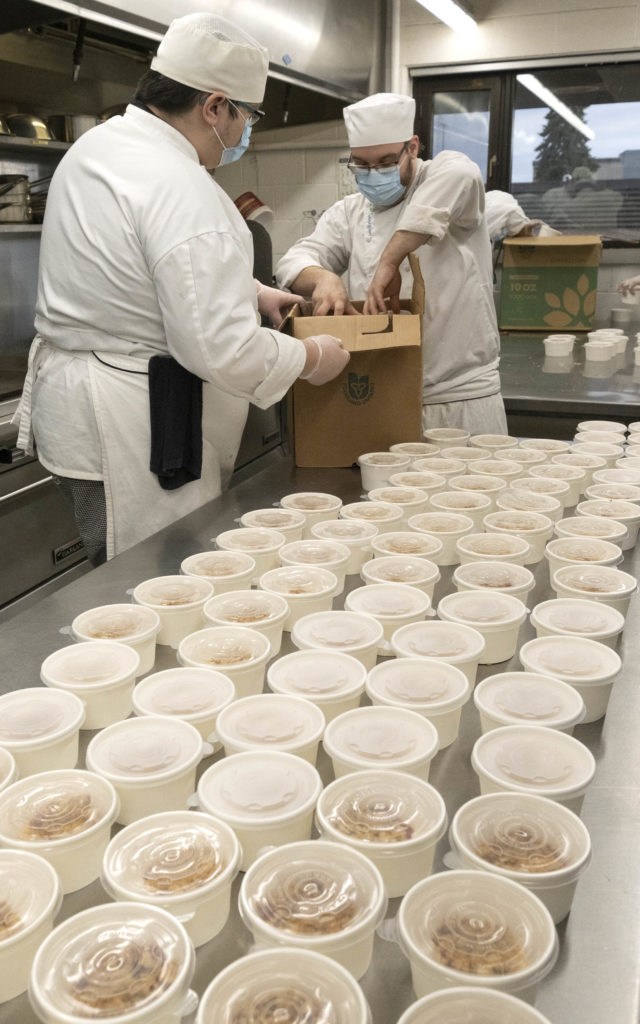 Two maleswearing white chef uniforms loading food into small white containers