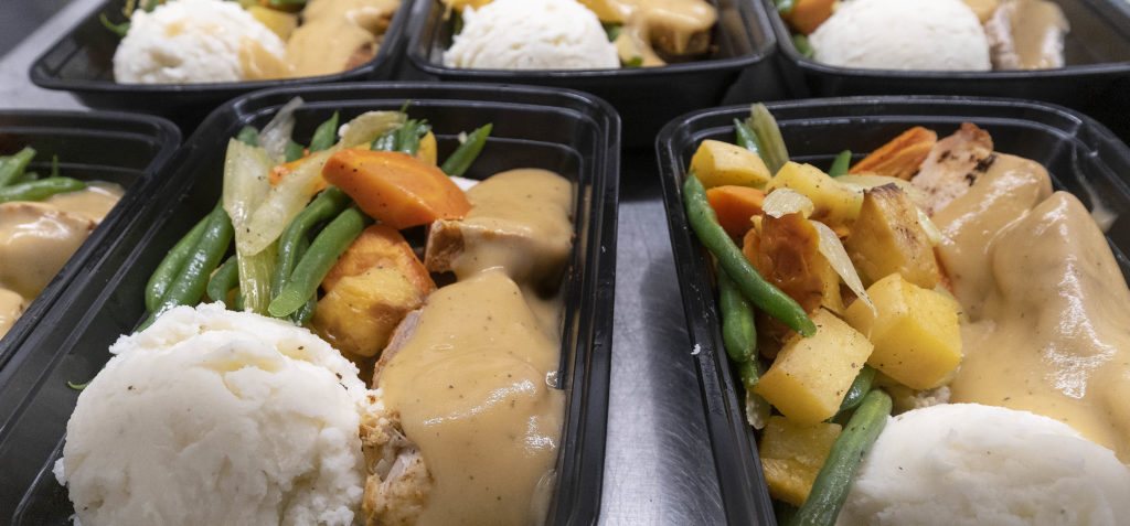 Black containers filled with a scoop of potatoes, vegetables and turkey and gravy