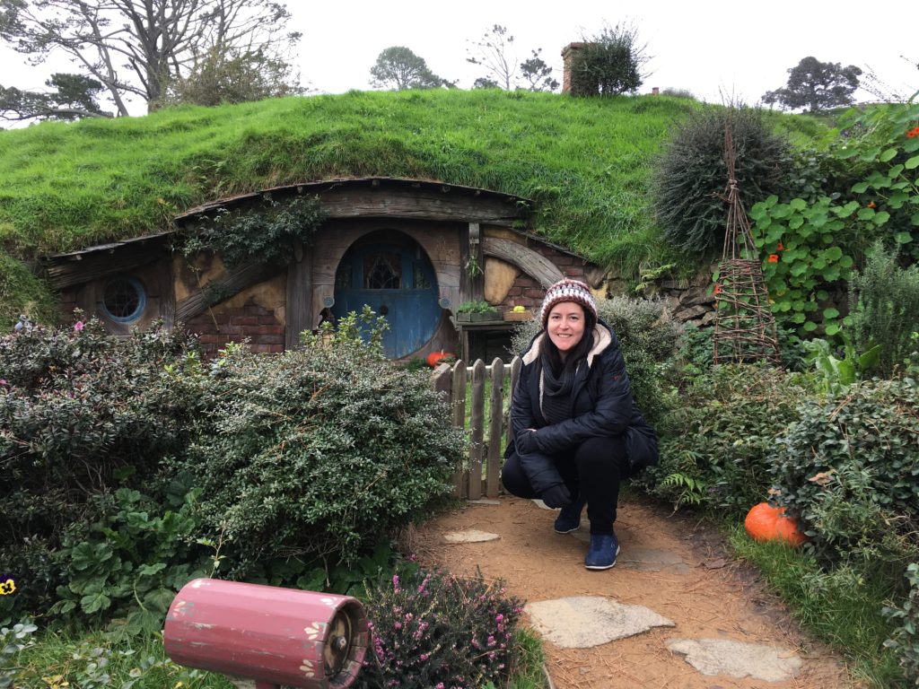 A person crouches down in front of the front door of a house build into a hill.