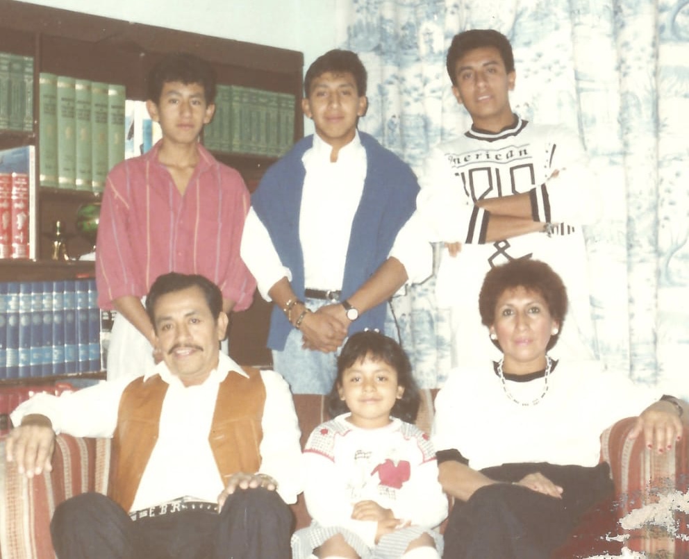 A family portrait showing three people sitting on a couch and three people standing behind them.