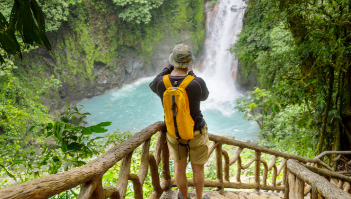 A person is standing on a platform facing a waterfall and taking photos.
