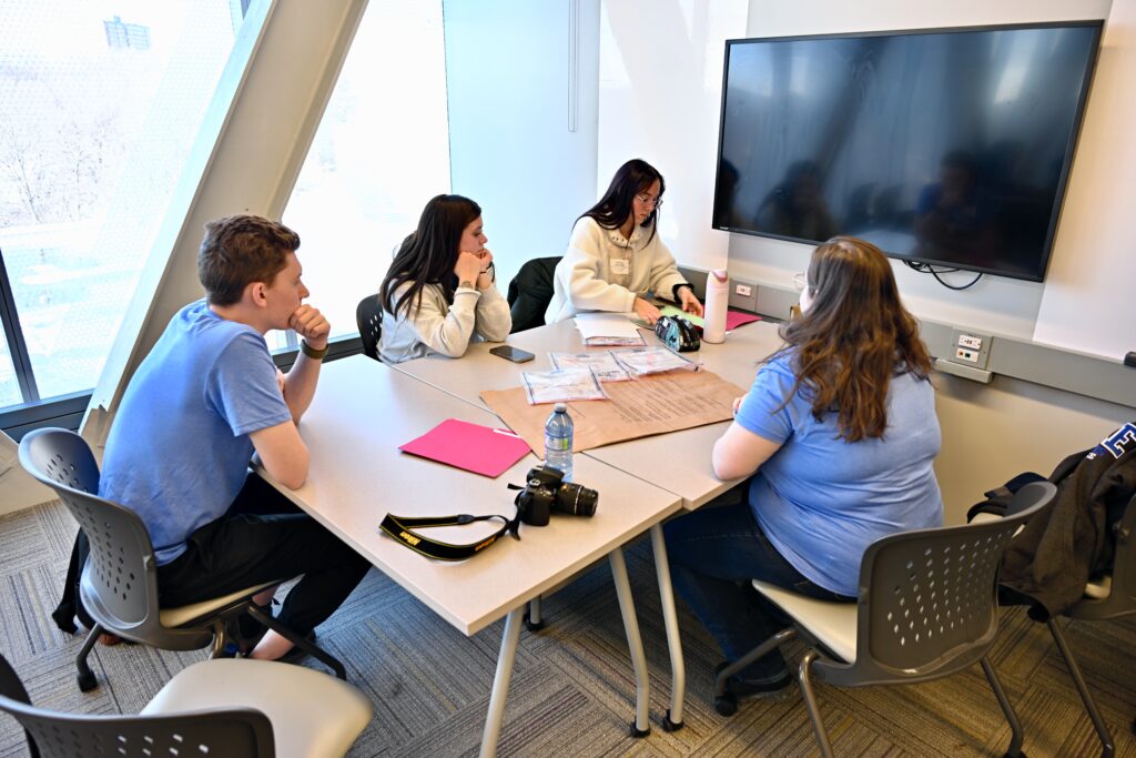 Four students sit around a table while looking at documents.
