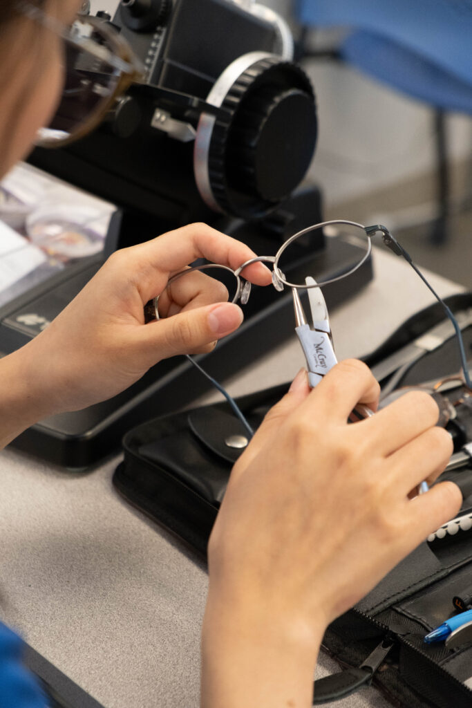A student uses a specialized tool to make adjustments to a pair of glasses.
