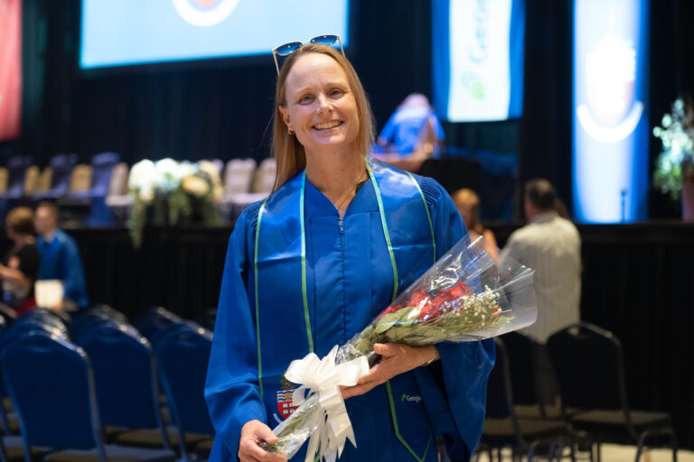 A Georgian grad holds flowers and smiles at convocation.