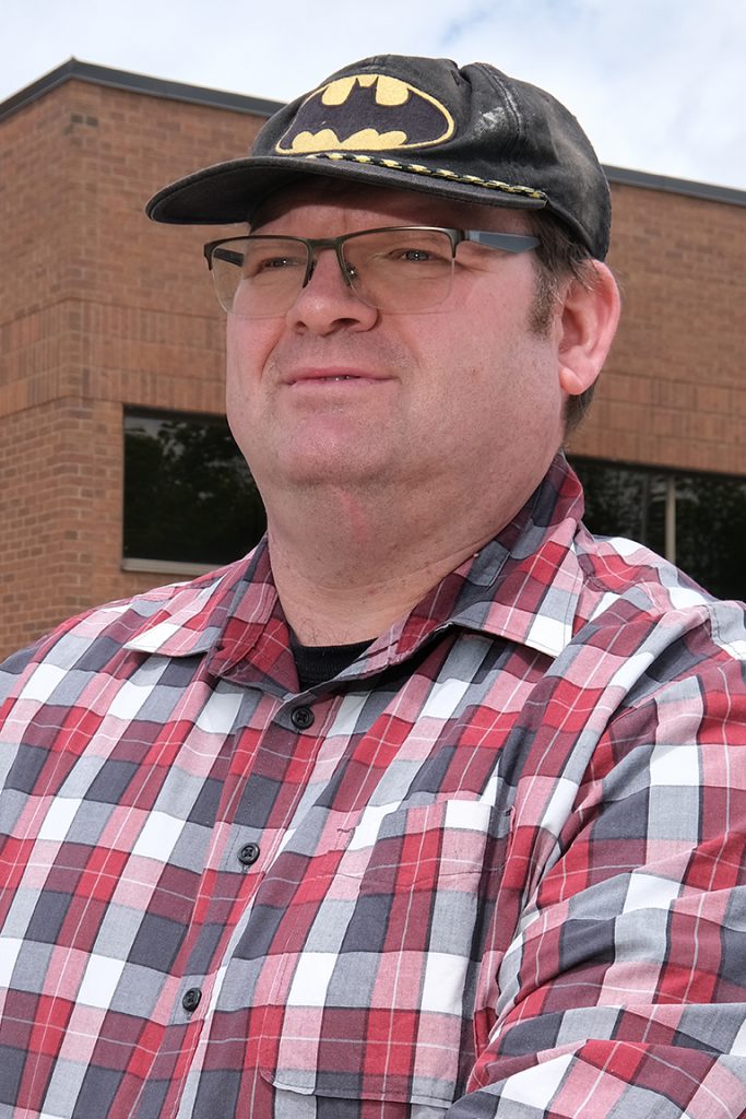 Person wearing a Batman hat stands at an angle and looks off in the distance.