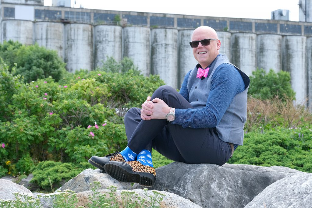 Person sits on rocks outdoors and smiles at the camera.