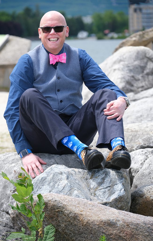 Person sits on some rocks outside and smiles at the camera.