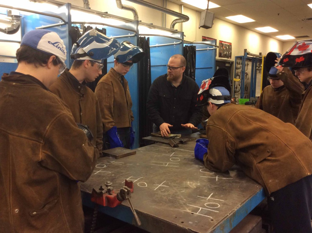 A group of students in welding masks in a shop.