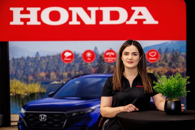 A woman wears a black t-shirt standing in front of a Honda sign.