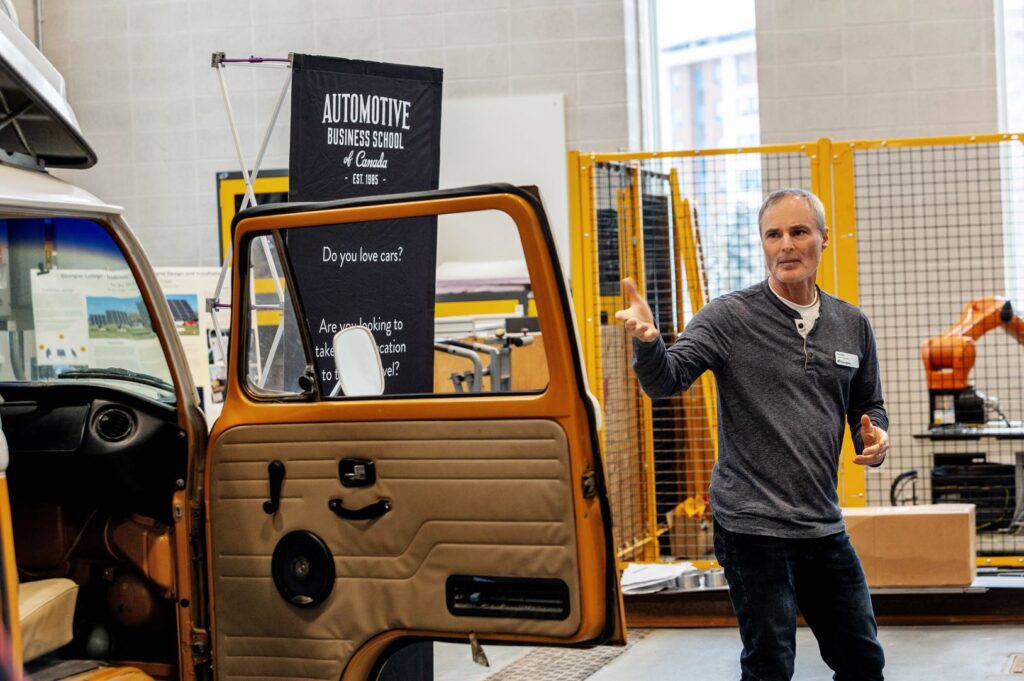 A person gestures next to a Volkswagen Westfalia camper van that is parked inside a work area.