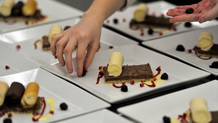 Hand placing a blackberry to garnish a fancy dessert