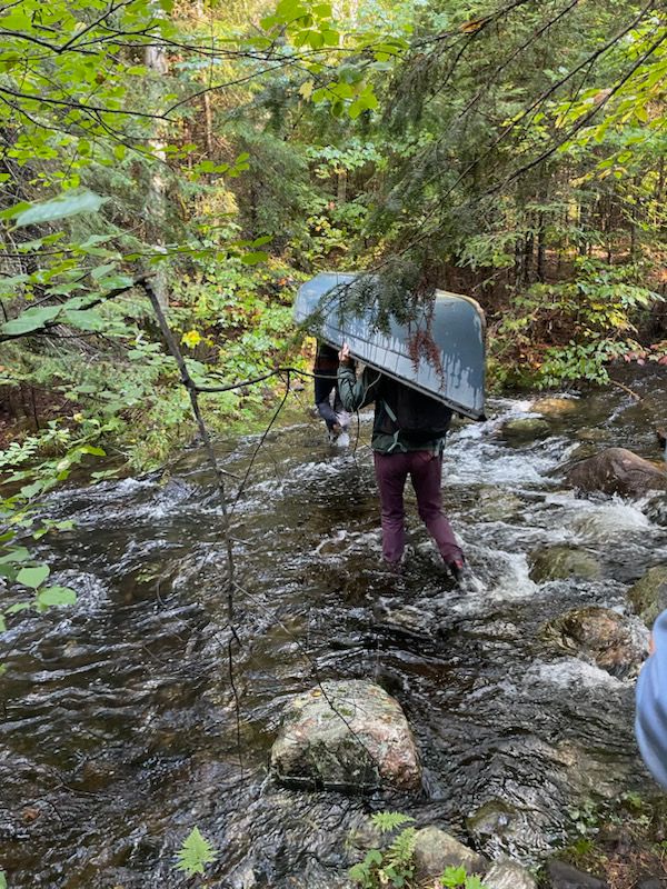 People portaging a canoe across a stream.