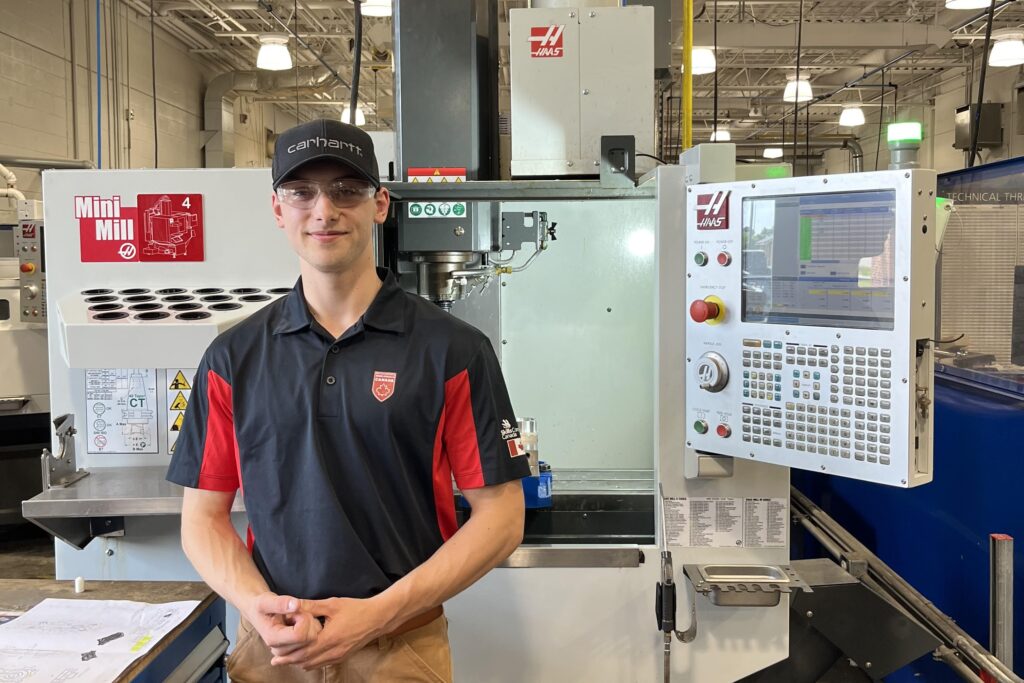 Ethan standing in front of precision skills equipment in a skills lab