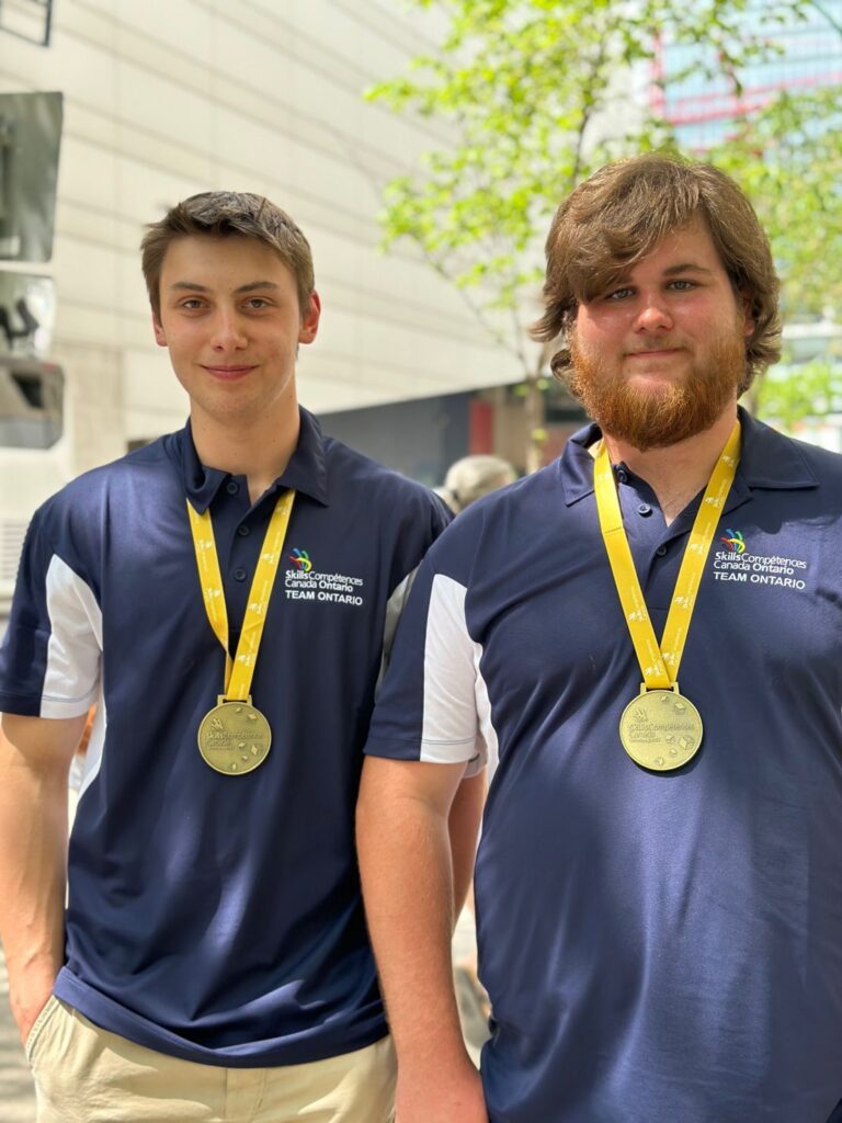 Two people wearing blue shirts with gold medals around their necks at the Skills Canada competition.
