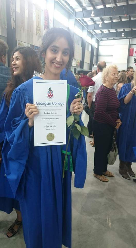 A woman holds her diploma and a rose at her graduation ceremony