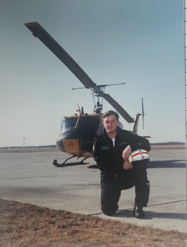 Military-Connected Campus Coordinator, Geoff Wall, kneeling in front of one of the helicopters he flew during his time with the RCAF