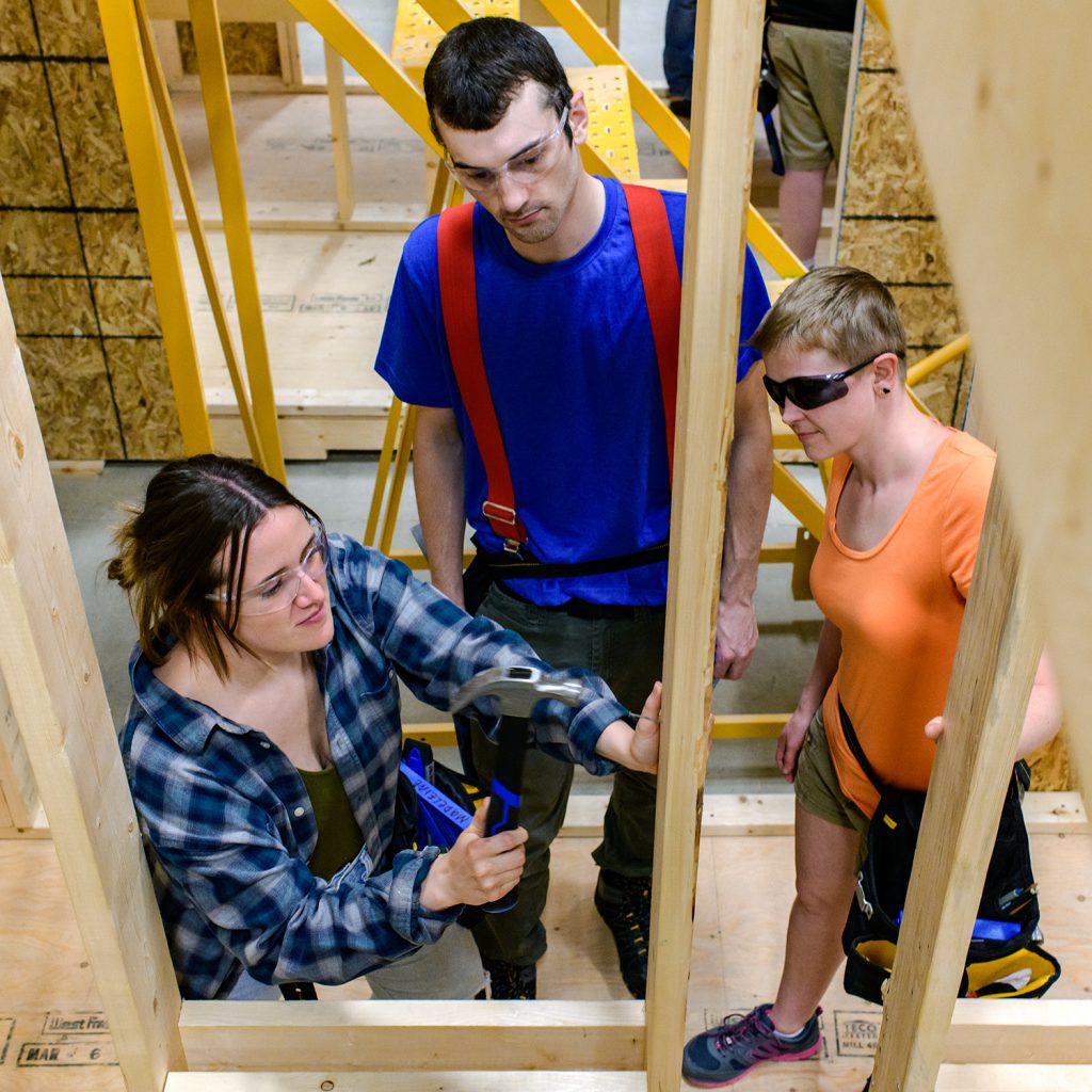Three young people (one male and two females) standing around in a framed in building.
