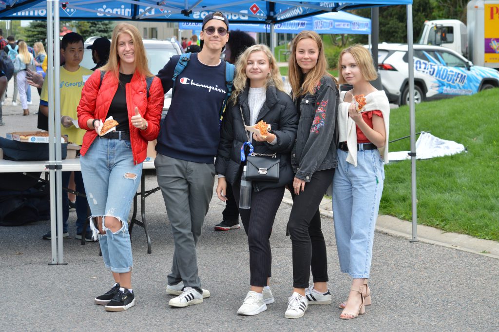 5 students smiling while holding pizza