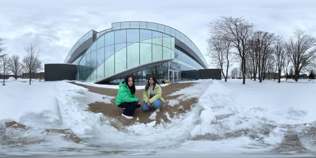 Two people sitting in the snow in front of a building. 