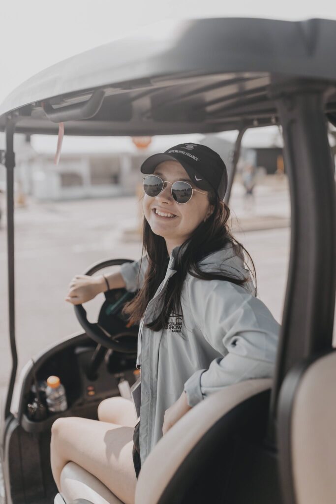 A person sits in a golf cart and looks back over their shoulder to smile at the camera.