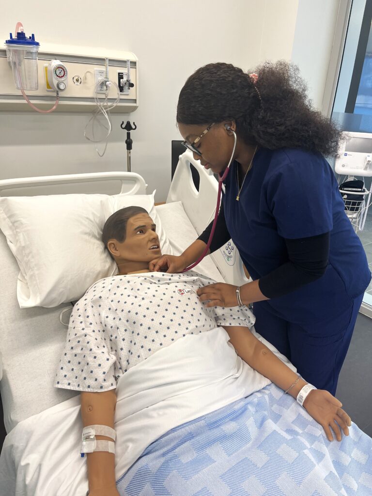 Kumbimi Agosu, a student in Georgian's nursing degree program poses with a manekin in a lab space.