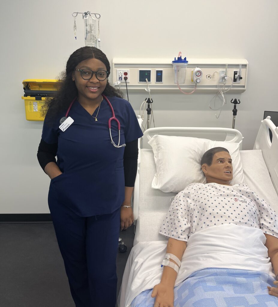 Kumbimi Agosu, a student in Georgian's nursing degree program poses with a manekin in a lab space.