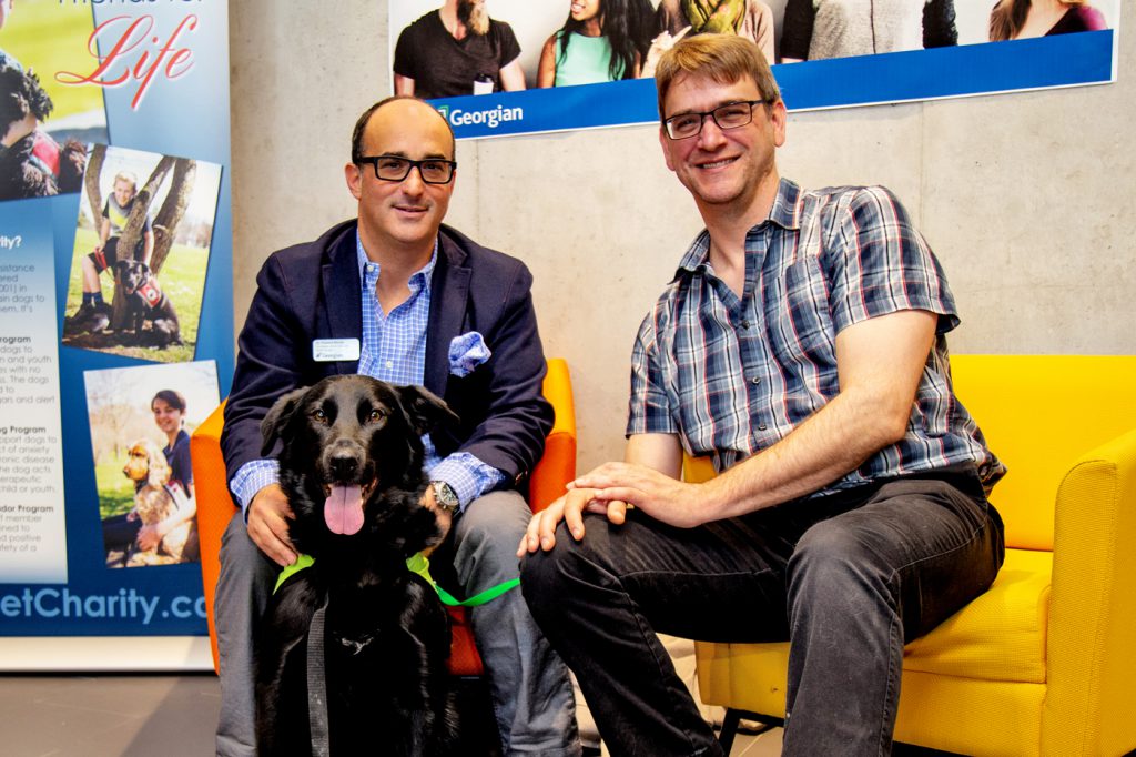 Two faculty sitting with a dog