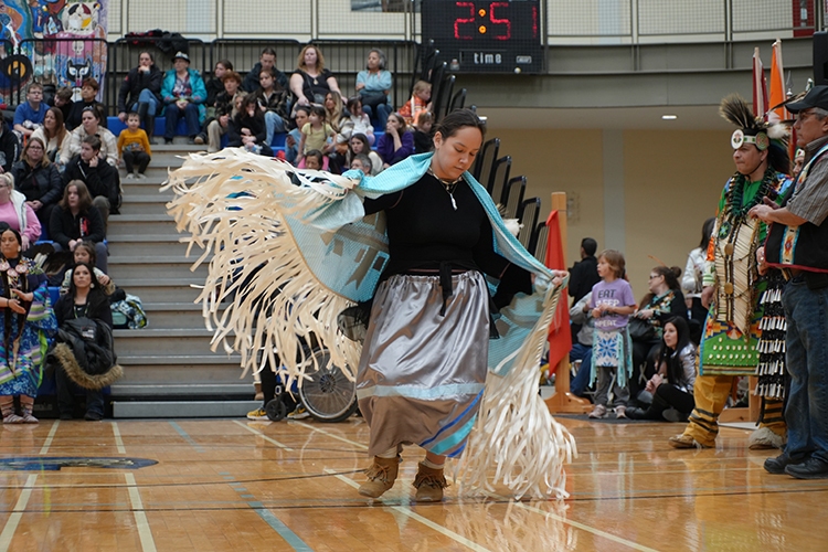 Dancers dressed in Indigenous regalia dancing in a gym